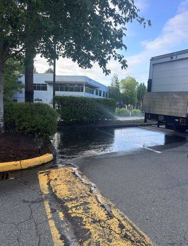 A sprinkler spraying across a commercial parking lot, with water pooling and running along the curb.